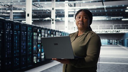 Engineer using laptop in data center, integrating new technologies and systems. Worker using notebook to oversee server hub, ensuring compliance with industry standards, camera A