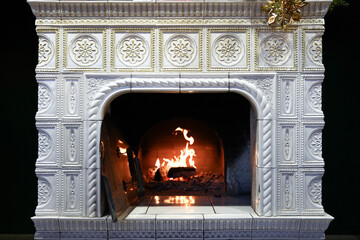 Vintage ornate ceramic fireplace with burning firewood and decorative tiles in cozy interior