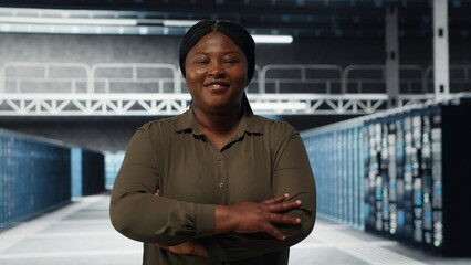 Portrait of smiling data center admin conducting security audit to protect against cyber threats. Happy supervisor walking in server room, pleased by compliance with industry standards, camera B