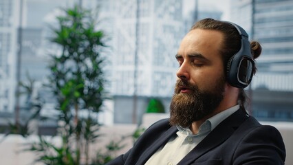 Male leader relaxes during a work break using sound healing to reduce stress. CEO with a calm and strong posture reflecting the power of meditation in a high performance company setting. Camera B.