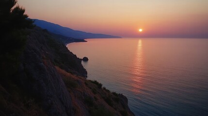 Coastal sunset over tranquil ocean.  Rocky cliff meets the sea at golden hour