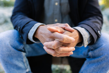 Close-up of adult man clasping hands in urban park. Still moment captured with natural outdoor atmosphere. Lifestyle and wellbeing concept.