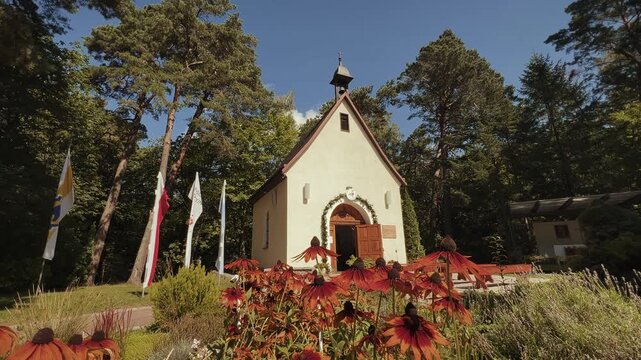 Sunny horizontal view of the "Sanktuarium Matki Bożej Trzykroć Przedziwnej" in Koszalin on Chełmska Mountain featuring rudbeckia flowers and the Polish flag
