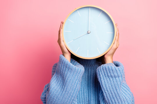 Young woman holds a large pastel clock over her face against a pink background to convey time awareness and casual fashion style in a lifestyle advertising image