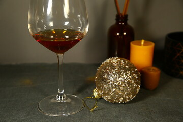 Glass with fresh gold brandy and Christmas golden ball, wax candle on holiday decor background with empty copy space. Closeup