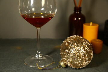 Glass with fresh gold brandy and Christmas golden ball, wax candle on holiday decor background with empty copy space. Closeup