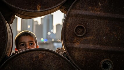A curious child peeking through a rusted oil drum Power, Oil, Dispute and Domination.