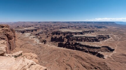 Vast arid landscape displays deep canyons and weathered rock formations under a clear blue sky