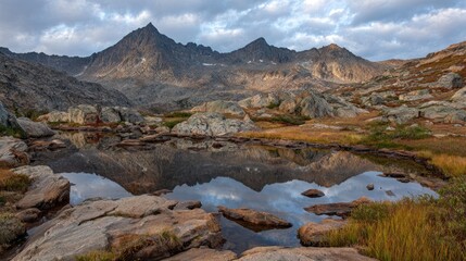 Rugged alpine peaks reflect in a still, clear tarn surrounded by barren landscape