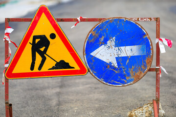 Construction road signage with arrow and warning symbol on asphalt background
