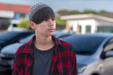 A quiet moment of melancholy. This middle schooler, dressed in a red plaid shirt and a grey knit hat, stands alone with a sad, introverted expression. Capturing the complexity of youthful solitude.