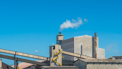 Industrial factory with conveyors and a smoking chimney. Modern manufacturing plant architecture in bright daylight