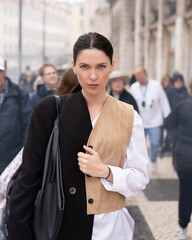Confident woman in trendy outfits walking on busy city street holding purse with serious and professional expression during daytime