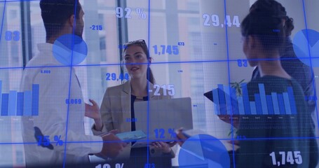 Presenting woman in blazer holding laptop as team reviewing glass dashboard in office with tablet