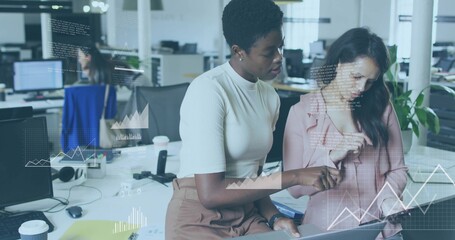 Pointing, two women analyzing data charts on laptop at open office, in white top, pink blazer