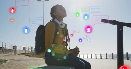 Sitting woman wearing yellow sweater with headset holding sandwich on bench by sea with chat icons