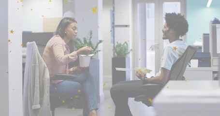 Eating two coworkers wearing pink blouse and light shirt, sitting in office aisle, holding takeout