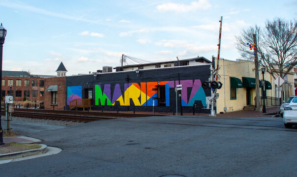 Colorful Large Marietta Town Mural Painted on a Dark Brick Wall Located Near Railroad Tracks in a Historic Downtown Area Under a Clear Blue Sky, Perfect for Travel and Local Tourism Promotion.