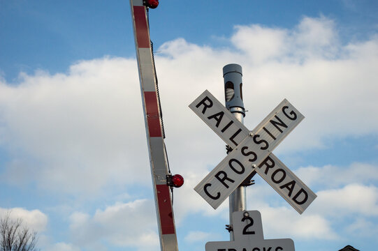 Close-up of a railroad crossing crossbuck sign with red signal lights against a blue sky, industrial transportation safety warning signal for railway tracks, public safety and transit concept.