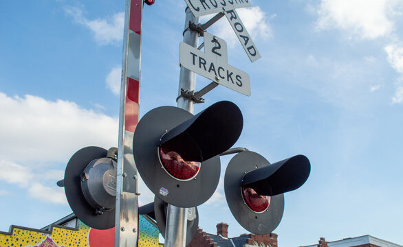 Close-up of Railroad Crossing Signal Lights and Signs Against a Bright Blue Sky with Soft Clouds, Warning Drivers and Pedestrians of Approaching Trains at a Level Crossing Intersection.