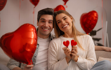 Happy young couple celebrating Valentine's Day holding red hearts and heart shaped balloon at home