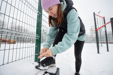Girl ties her sneakers on a sports field on a snowy sports ground in winter