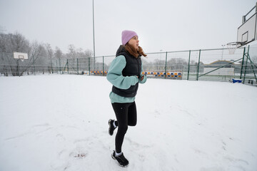 Girl performs a running in place exercise on a snowy sports ground in winter.