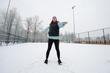 Girl doing a body rotation exercise with arm swings on a snowy sports field in winter.