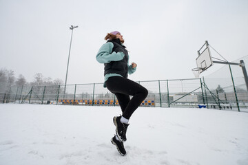 Girl performs a high-knee jog on a snowy sports field in winter.