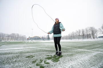 Girl jumps rope on a snowy football field in winter.