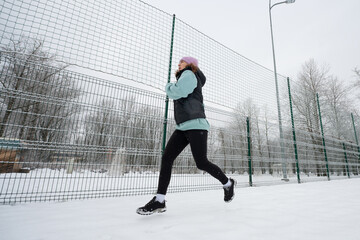 Girl runs on a snowy sports ground in winter.