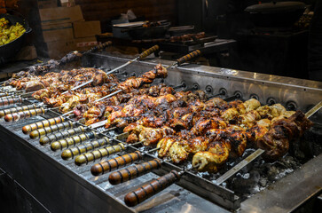 Grill is heavily loaded with skewers of various meats including shish kebab and chicken pieces charring over hot coals, ready for serving at a large outdoor food stall