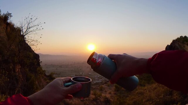Hiker pouring coffee from thermos at sunrise