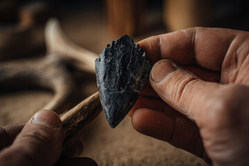 Obraz premium Obsidian arrowhead crafted from volcanic glass held by hands showing detailed texture and sharp edge in rustic setting with natural light