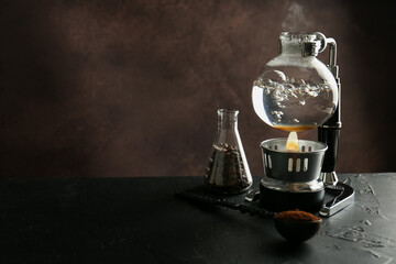 Siphon (vacuum) coffeemaker with hot water on black table against brown background, closeup. Space for text