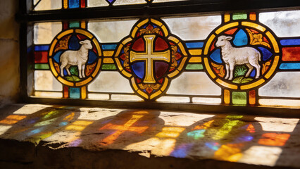 Stained glass window depicting cross and lambs with colorful reflections  
