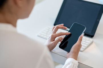 Hands of business woman using blank smartphone with tablet and keyboard on table