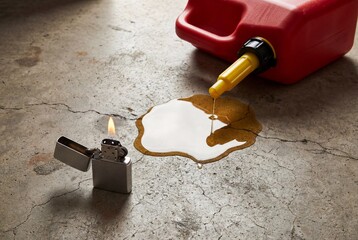 Silver lighter with open flame standing near spilled gasoline and red canister on cracked concrete