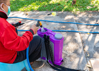 A worker prepares a purple backpack sprayer, rinsing the filter with water before applying chemicals.