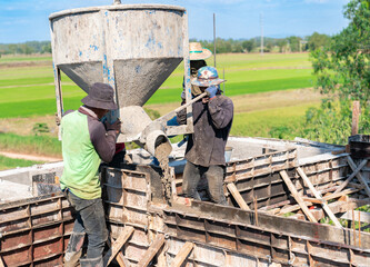 Construction workers pouring wet concrete from a bucket into a foundation formwork
