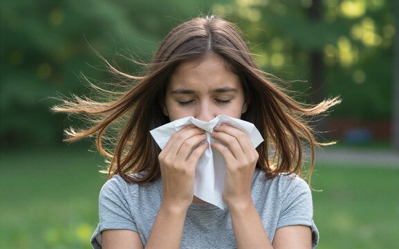 Woman outdoors, blowing nose with tissue, wind tousling her hair.