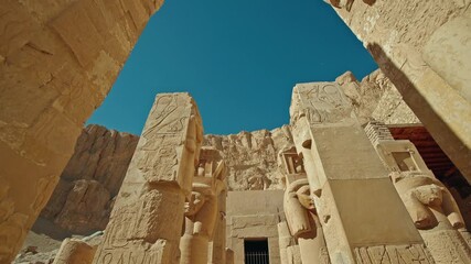 Stone columns and carved reliefs of the Temple of Hatshepsut in Deir el Bahari, Luxor, ancient Egyptian architecture set against limestone cliffs and clear blue sky
