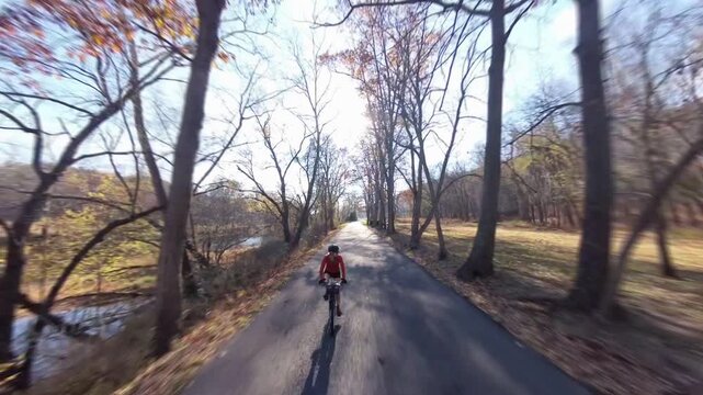 A woman bikes along a winding road near a river in West Virginia. Autumn leaves surround her on this beautiful day.