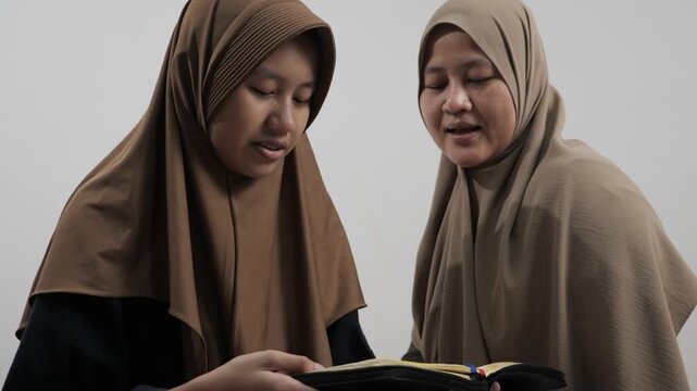 Asian Muslim mother teaching her daughter how to read the Quran at home