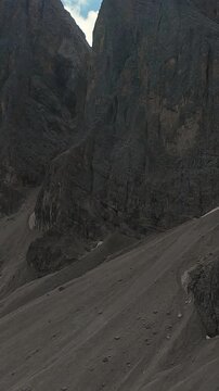 Vertical Screen Steep Scree Slope Beneath Sheer Cliff, Stark Talus Field And Towering Limestone Wall With Sparse Vegetation And Textured Rock Strata Remote High Alpine Basin, WindSwept