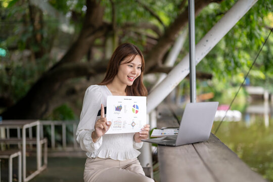 Asian businesswoman presenting charts during remote video call outdoors - Powered by Adobe