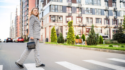 Business woman engineer crossing street near modern residential buildings in spring. Urban construction planning and professional project management.