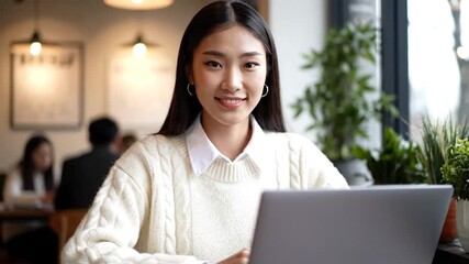 A woman in a cafe with a laptop. Plants and other patrons are out of focus