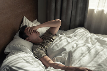 tired sleepless man in bed with hand over face, portrait of sad male alone. insomnia, hangover, fear, sadness, abuse, depression, addiction.