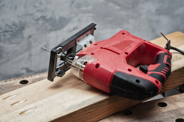 Naklejka premium Red electric jigsaw on a wooden plank and workbench. Power tool for professional use. Woodworking process and DIY craftsmanship in a workshop setting.